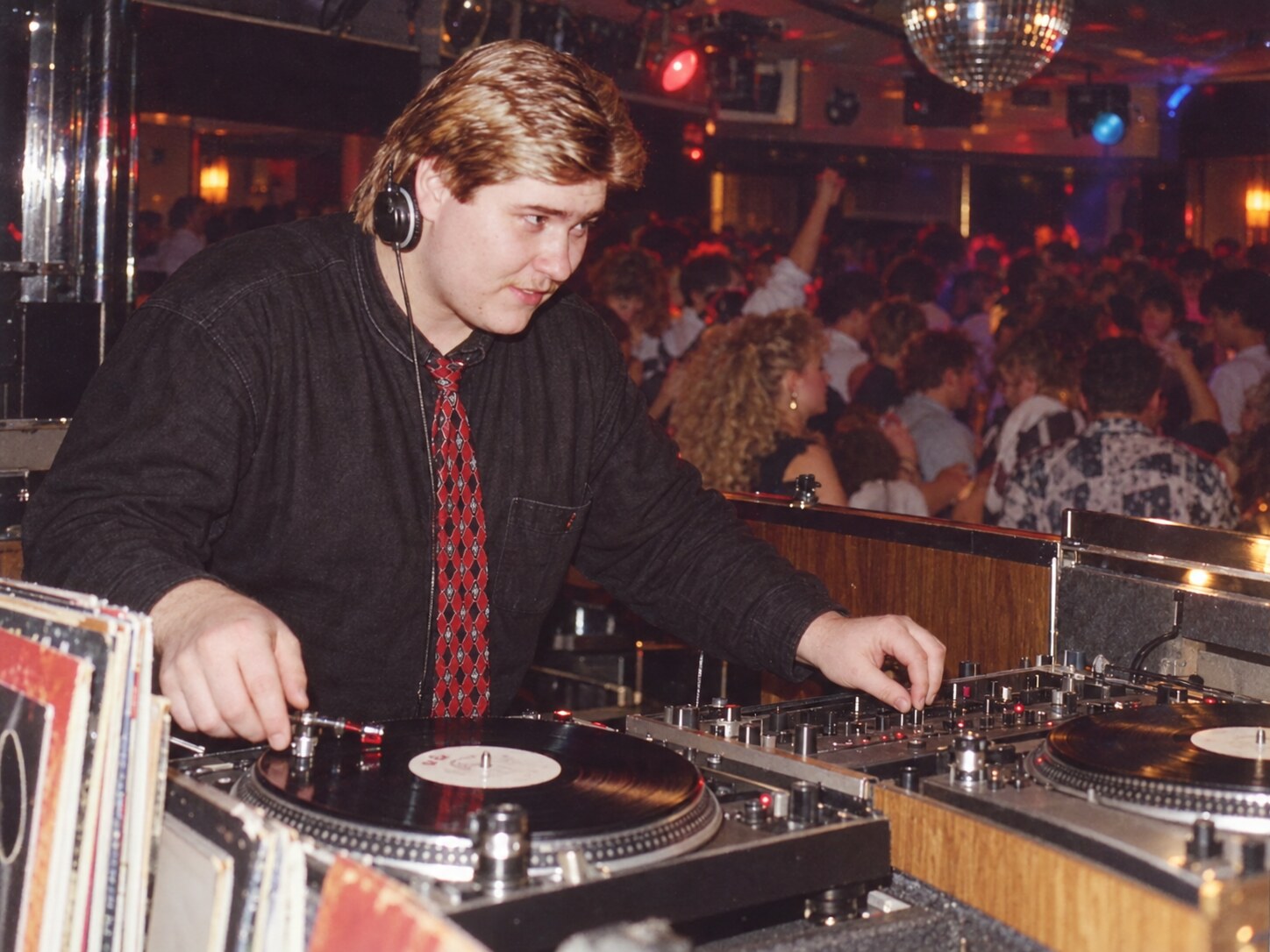 DJ Tommy Anfang der 1990er-Jahre an zwei Plattenspielern vor einer vollen Tanzfläche